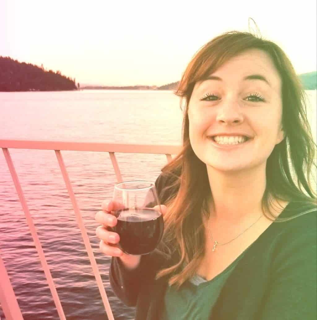 A woman enjoying a glass of red wine on a boat during sunset with a scenic water and forest background.