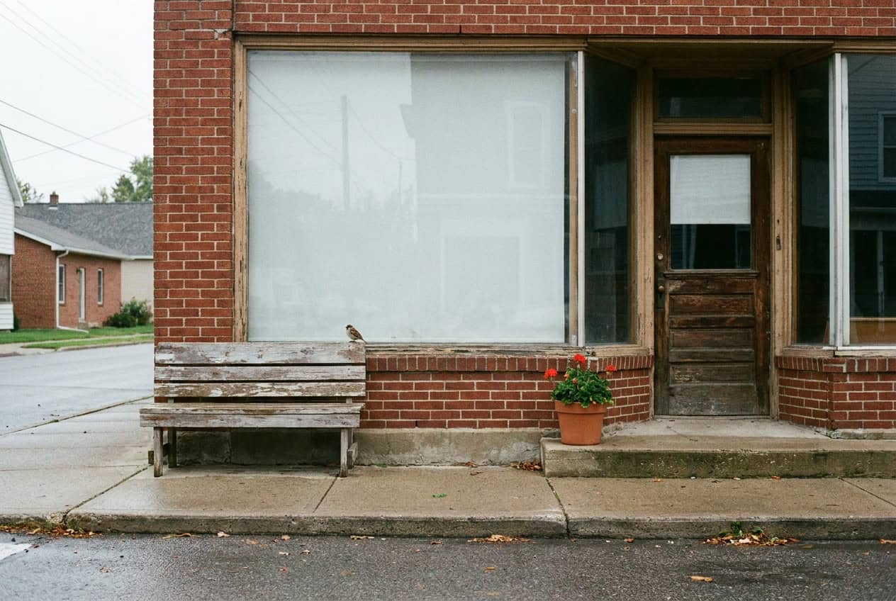 What a Professional Website Costs in the Midwest (Real Numbers) 1 A small brick storefront on a quiet Midwestern main street with a weathered bench, a red geranium in a terracotta pot, and a sparrow on the window sill